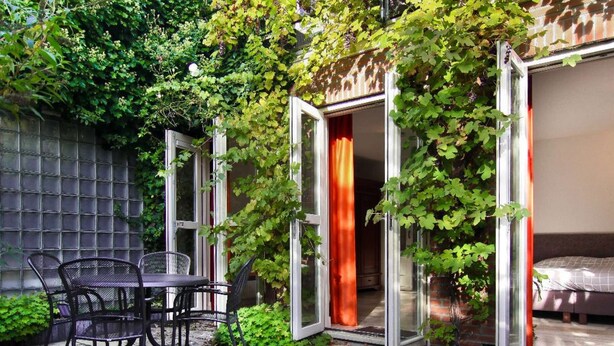 A patio with a table and chairs, a brick wall, and a glass door leading to a room.