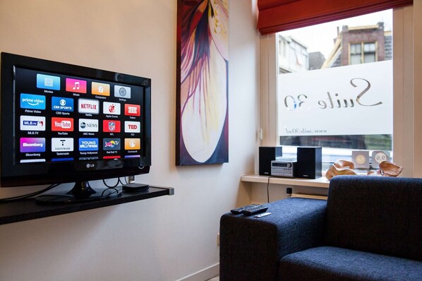 A living room with a flat-screen TV displaying various streaming services, a window with a view of buildings, and a piece of abstract art on the wall.