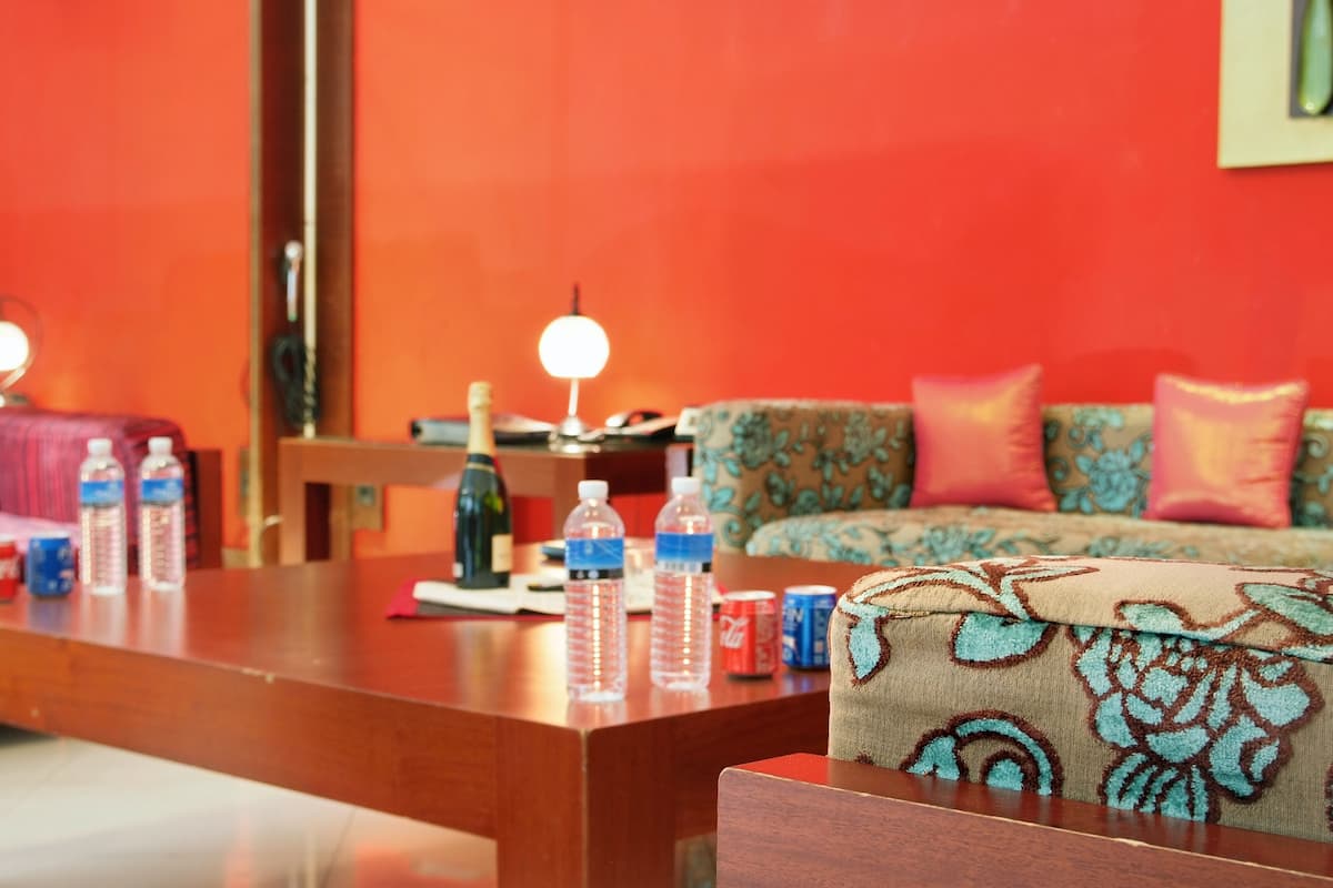 A hotel room with a wooden desk, two water bottles, a bottle of wine, a can of soda, and a sofa with patterned cushions.