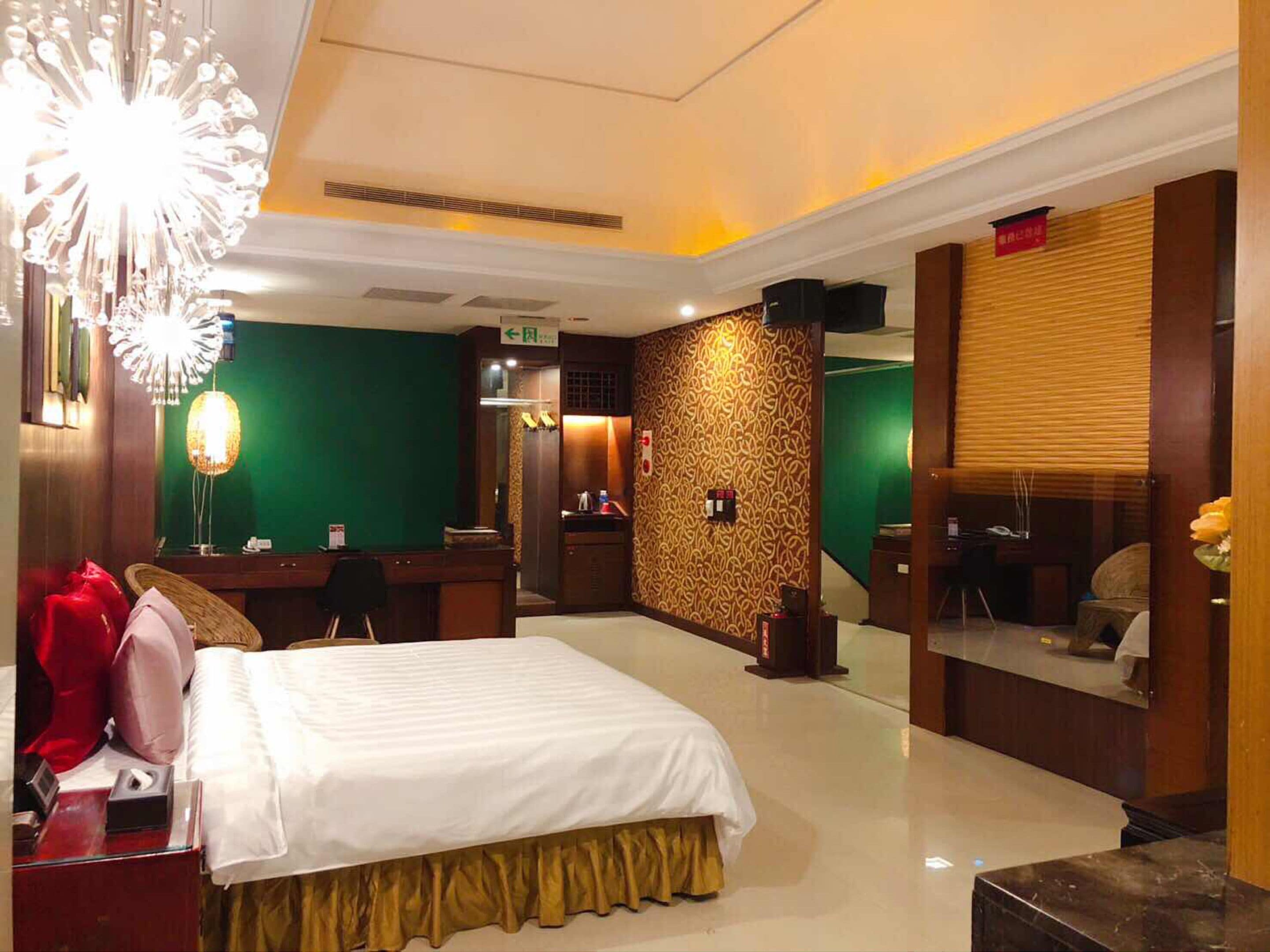A hotel room with a bed, a desk, a mirror, and a green wall with a patterned design.
