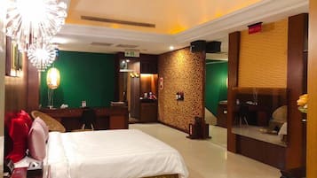 A hotel room with a bed, a desk, a mirror, and a green wall with a patterned design.