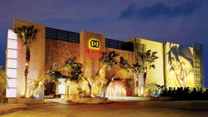A hotel with a prominent logo, palm trees, and a large illuminated billboard. - Q Motel (New Taipei City)