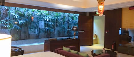 Una habitación de hotel moderna con una cama grande, un sofá, una mesita y vistas a un jardín tropical.