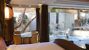 A hotel room with a large bed, a glass door leading to an outdoor seating area with chairs and a table, and a view of a stone wall and plants. - Q Motel (New Taipei City)