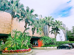 A building with a modern facade, palm trees, and a parking lot.