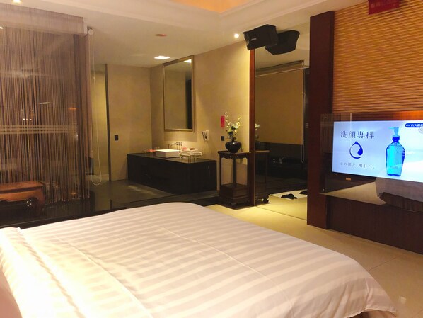 A hotel room with a large bed, a bathroom with a sink and mirror, and a television displaying an advertisement.