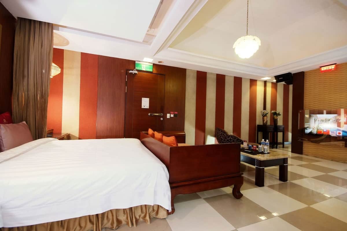 A hotel room with a bed, a wooden bench, a small table, and a reception desk.