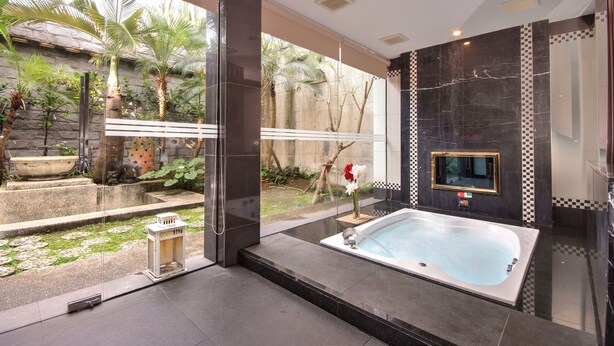 A modern bathroom with a large bathtub, a stone wall, and a view of a garden. - Q Motel (New Taipei City)