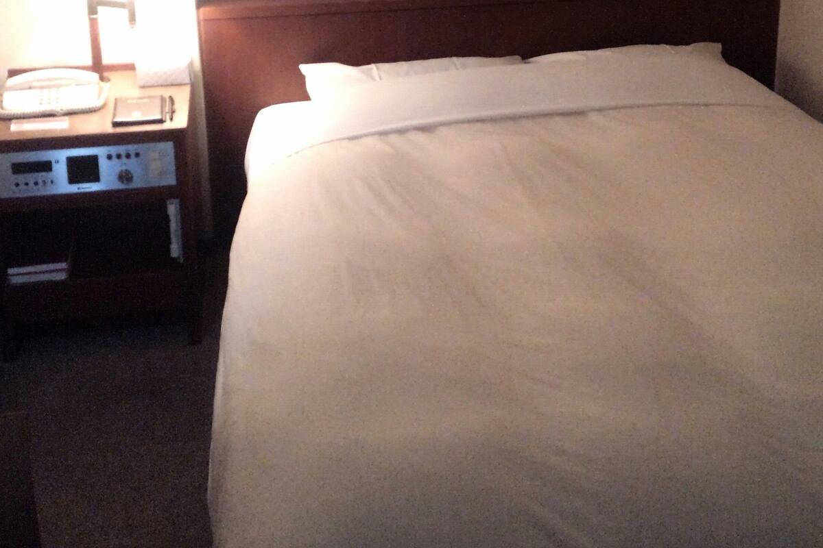 Ein Hotelzimmer mit einem ordentlich bezogenen Bett, einem Nachttisch mit Lampe und einem gerahmten Bild an der Wand.