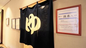 Un pasillo con un banderín negro que presenta un gran símbolo blanco, un cartel enmarcado con texto japonés y dos cuadros en la pared.