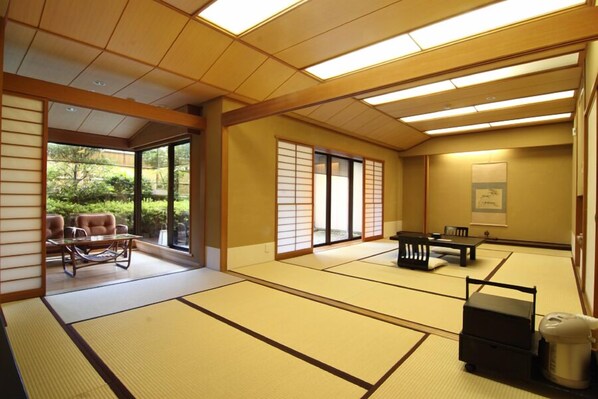 Habitación con suelo de tatami, puertas correderas, una mesa de tatami, una mesita baja y decoración tradicional japonesa, con vistas a la vegetación exterior.