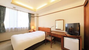 Une chambre d’hôtel équipée d’un lit, d’un bureau, d’une chaise, d’une télévision et d’un petit réfrigérateur.