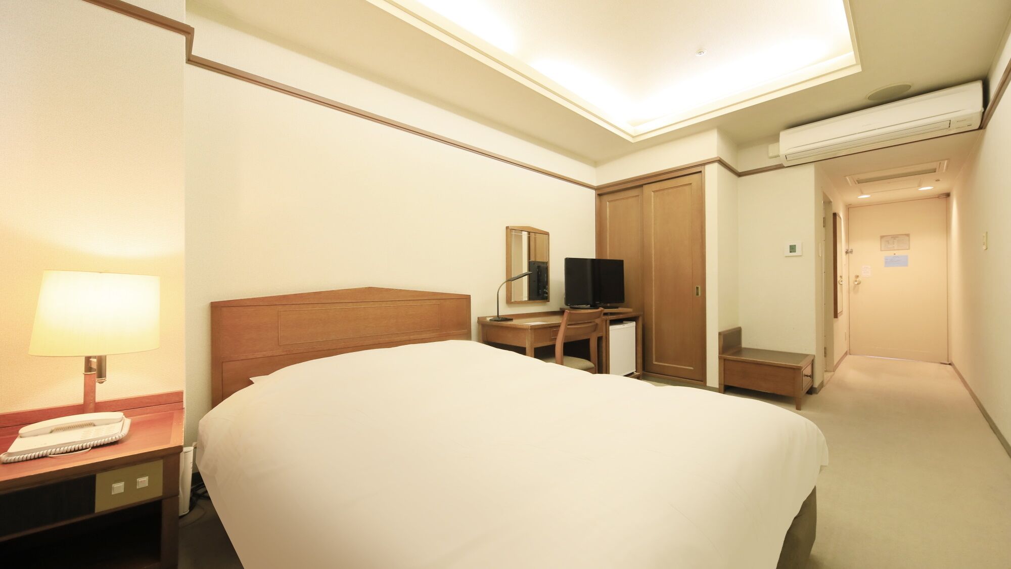 A hotel room with a bed, a desk with a computer, a TV, and a lamp.