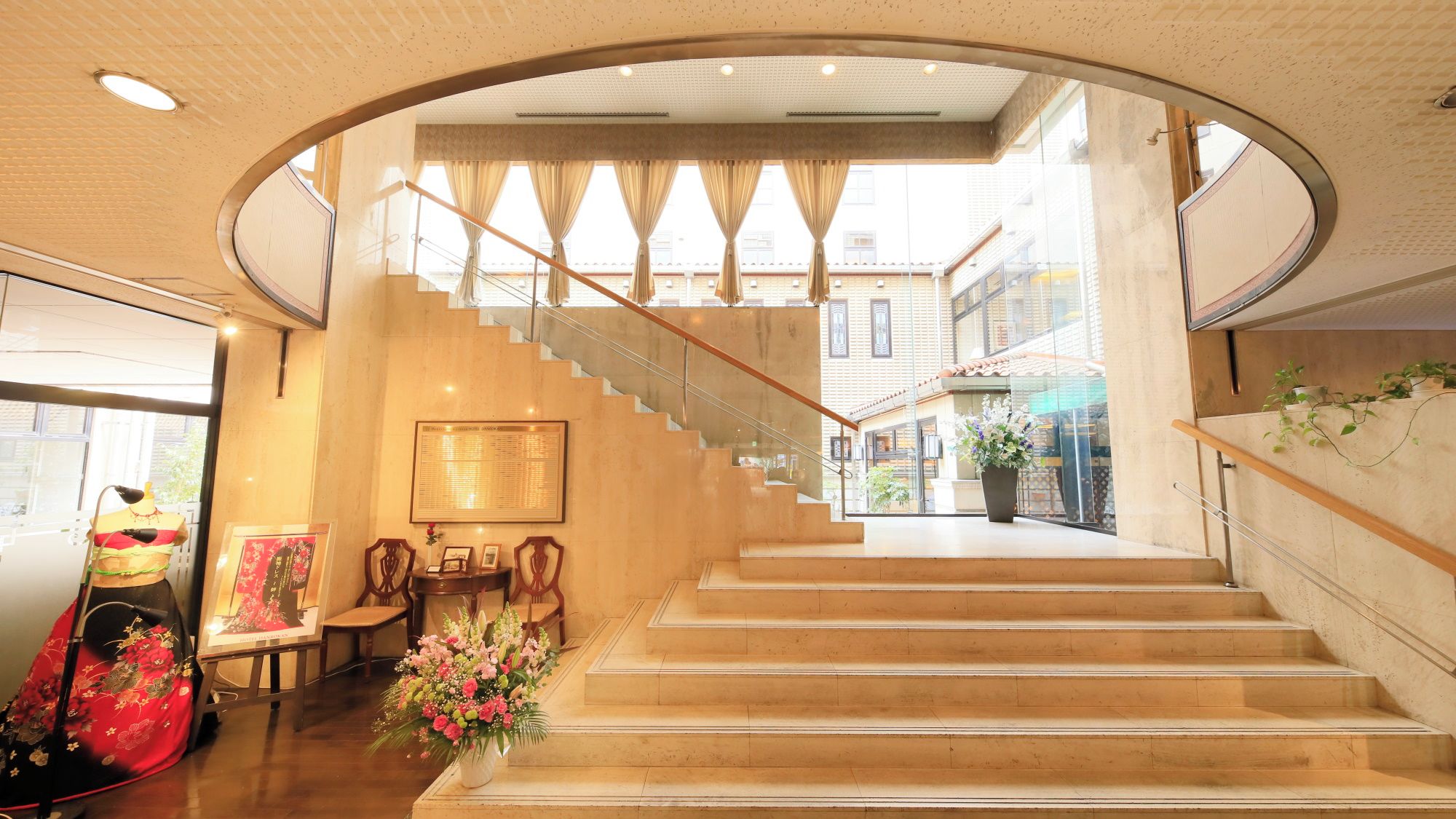 A modern interior with a staircase leading to an upper level, a mannequin with a dress, and a vase of flowers.