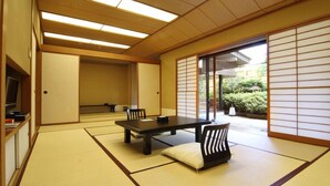 A traditional Japanese room with tatami flooring, a low table, chairs, and sliding doors. - Hotel Danrokan (Kofu)
