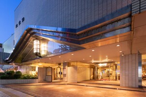 A modern hotel entrance with a glass facade, a covered walkway, and a well-lit lobby area.