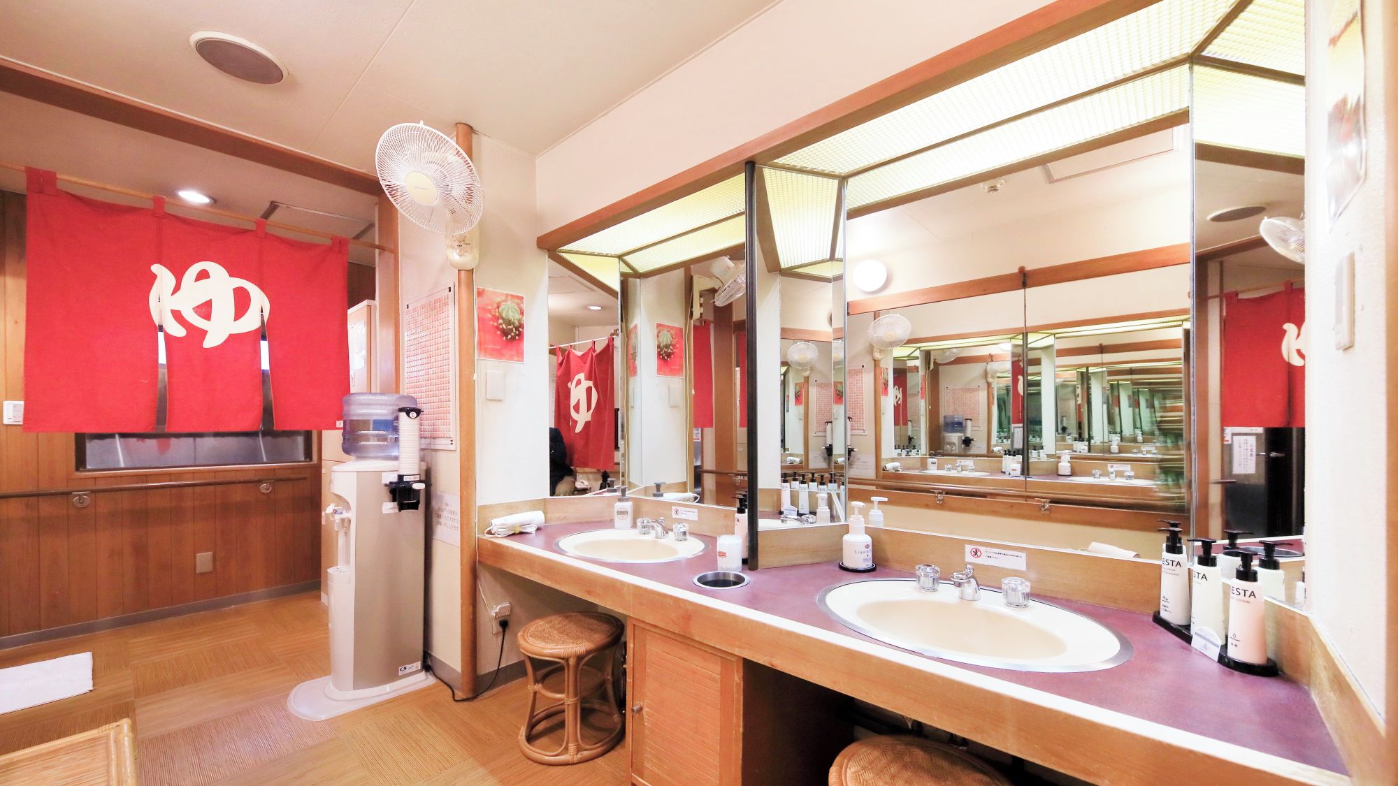 A hotel bathroom with two sinks, a large mirror, and a red wall with a logo.
