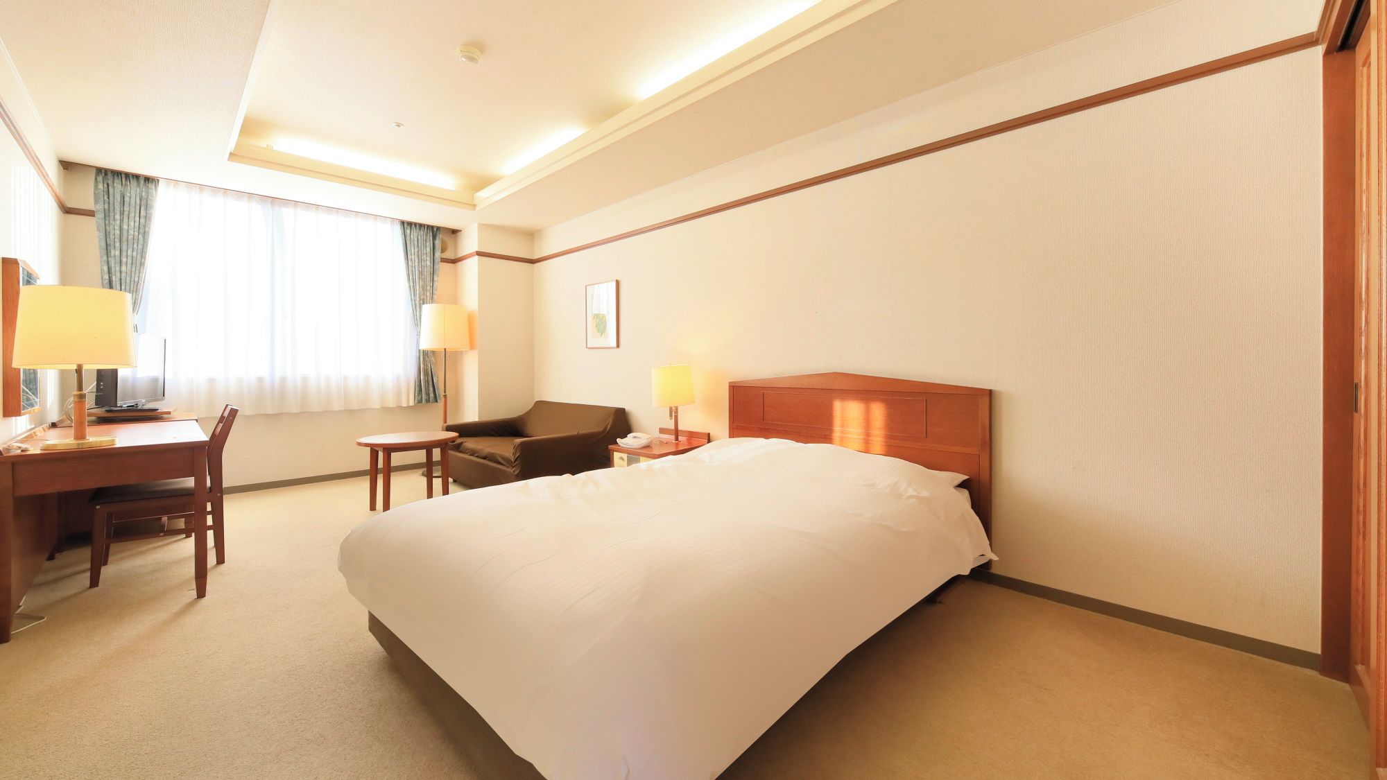 Ein Hotelzimmer mit einem großen Bett, einem Schreibtisch mit Stuhl, einem kleinen Tisch und zwei Lampen.