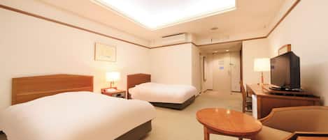 A hotel room with a large bed, a smaller bed, a desk with a television, and a ceiling light.