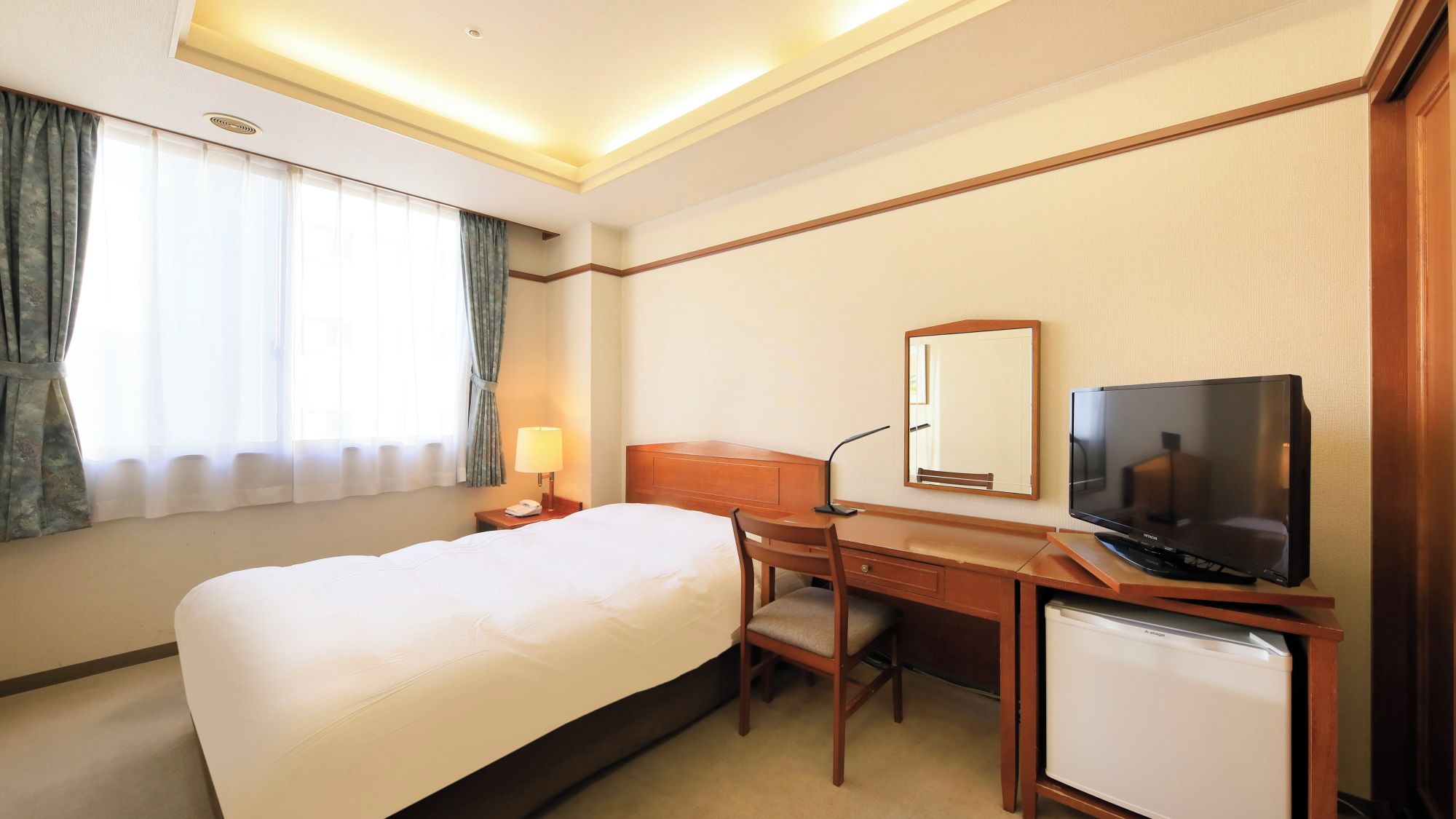 A hotel room with a bed, desk, chair, television, and a small refrigerator.