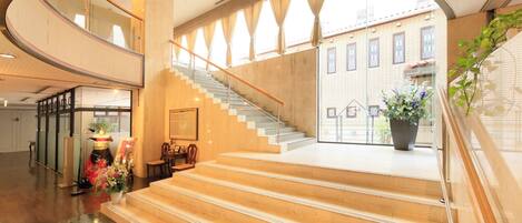 A hotel lobby with a grand staircase, a reception desk, and a view of the building outside.