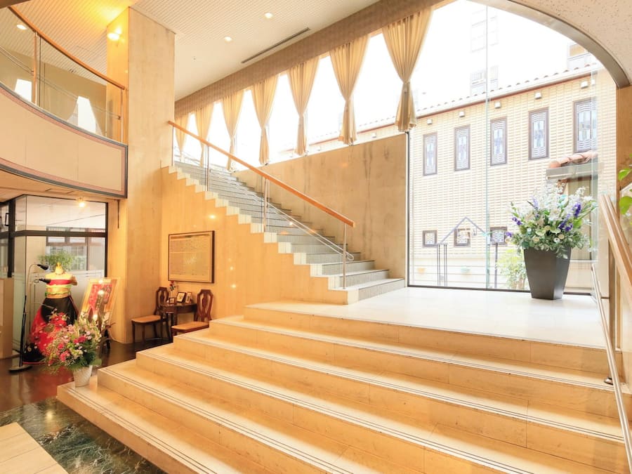 Un vestíbulo de hotel con una escalera monumental, una recepción y vistas del exterior del edificio.