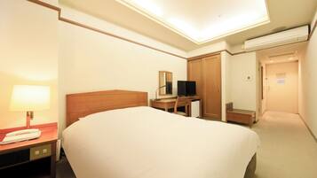 Habitación de hotel con cama, escritorio, silla, lámpara, televisión y aire acondicionado.