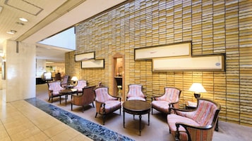 A hotel lobby with a seating area, a reception desk, and a wall with a textured pattern.