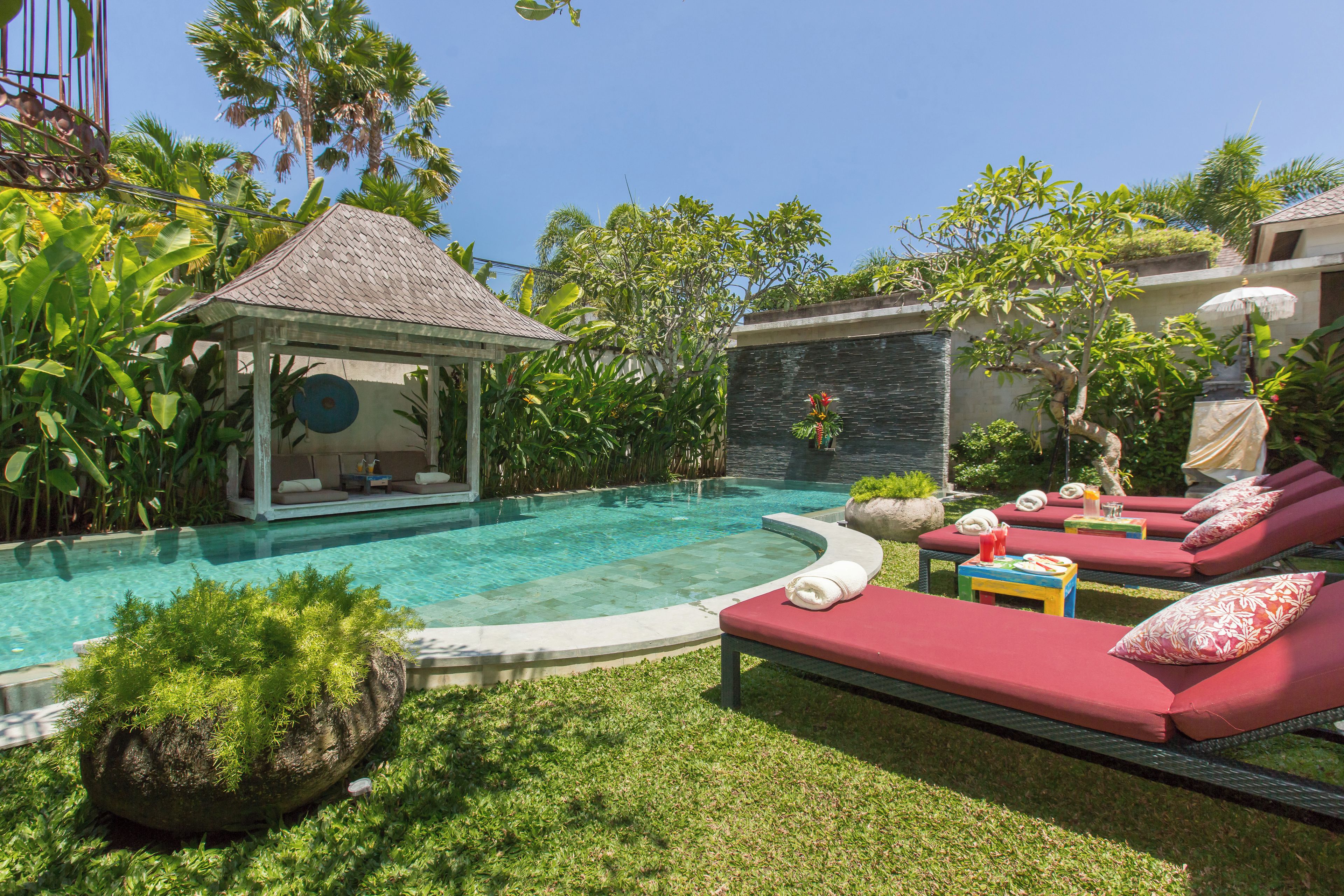A poolside area with lounge chairs, a small gazebo, and lush greenery.