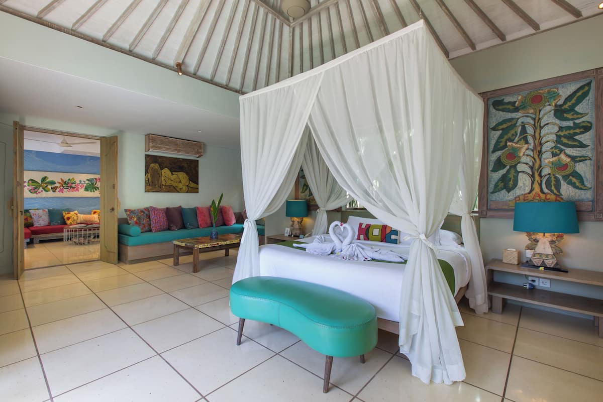 A spacious bedroom with a four-poster bed, a teal bench, and a colorful sofa.