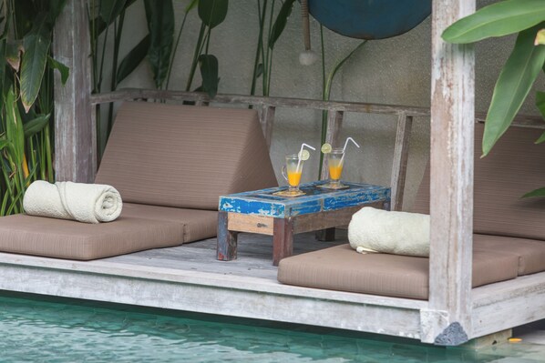 Un área de descanso junto a la piscina con dos sillones acolchados, una mesita con bebidas y una toalla.