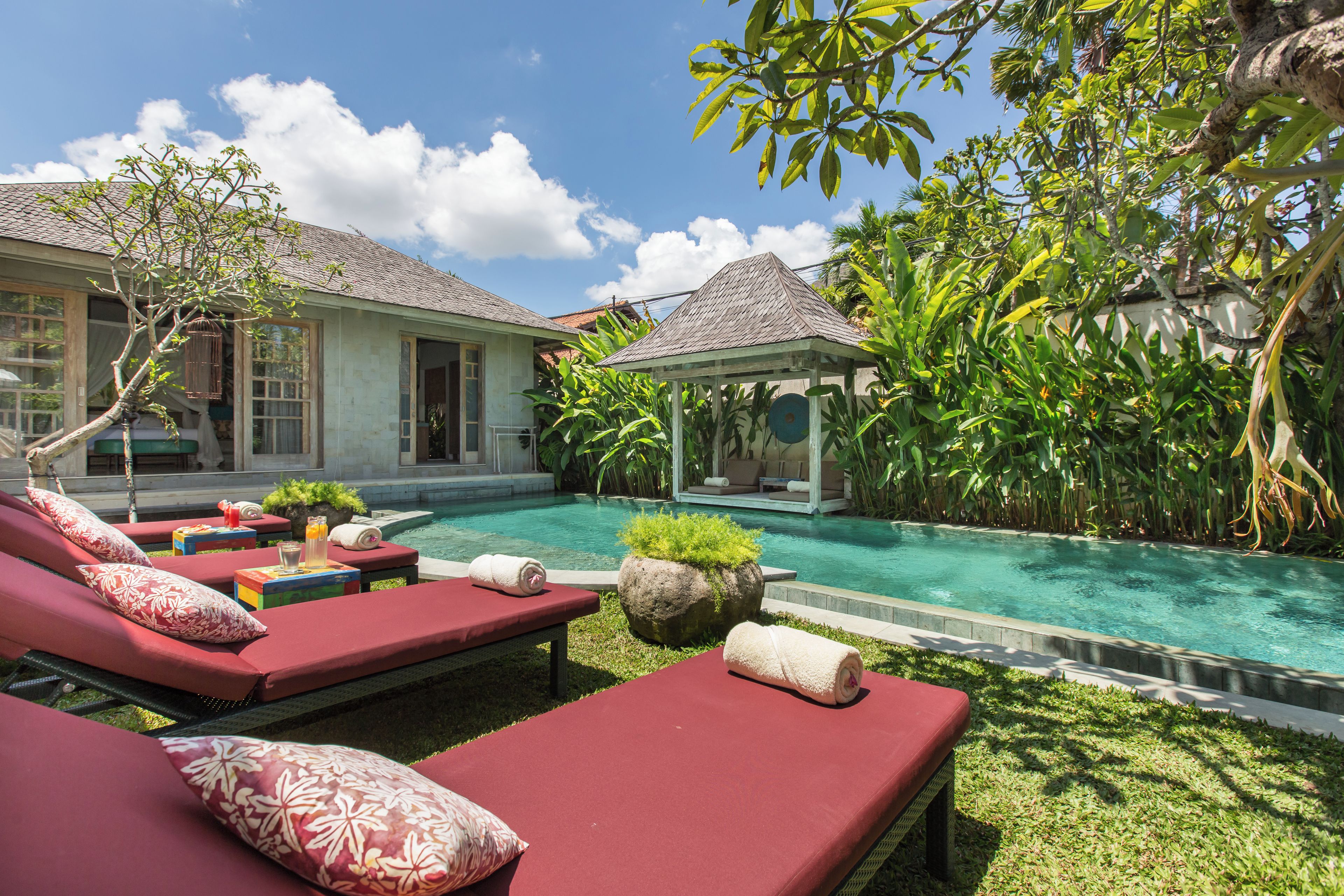 A poolside area with lounge chairs, a small gazebo, and lush greenery.