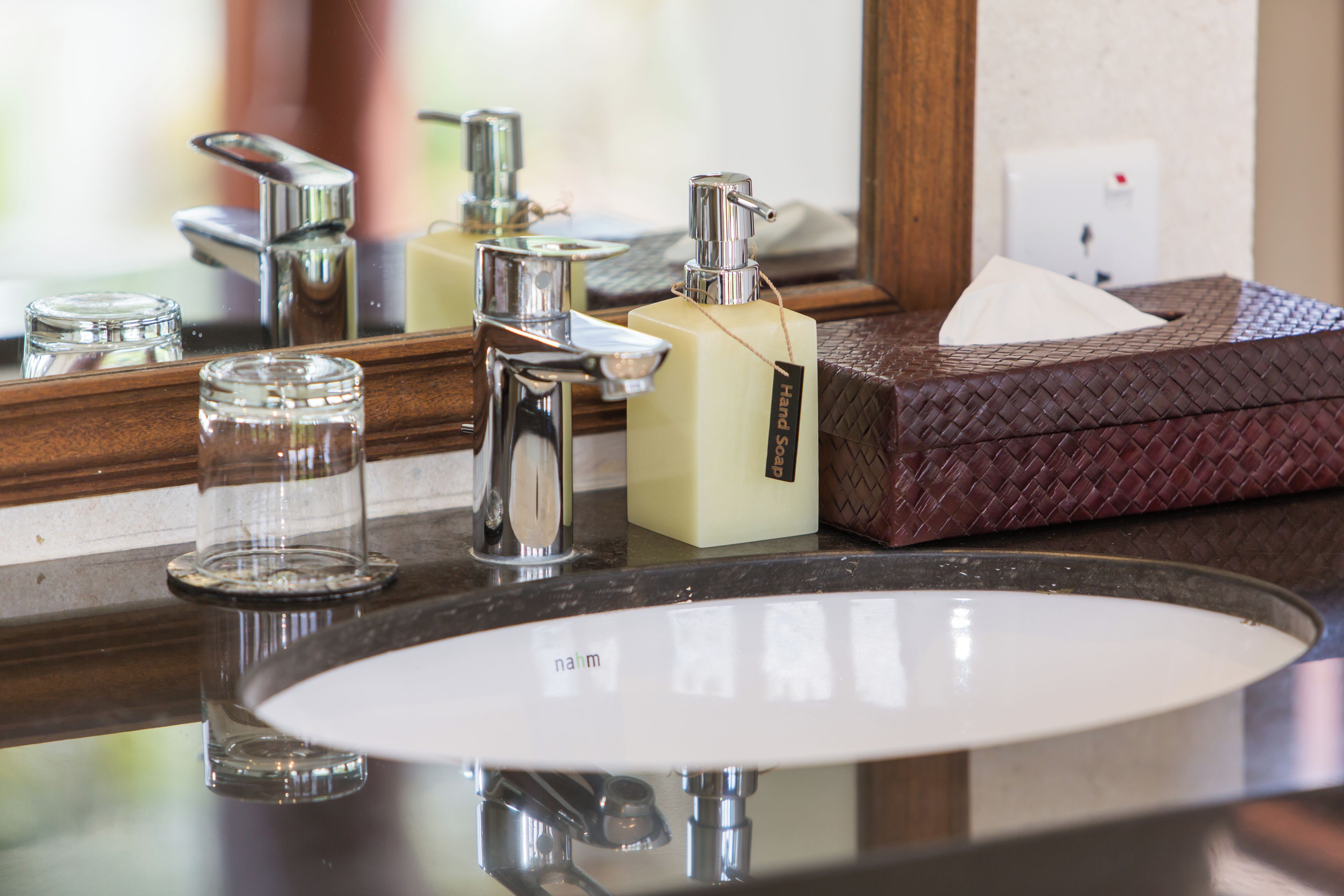 A bathroom sink with a mirror above it, a soap dispenser, and a glass.