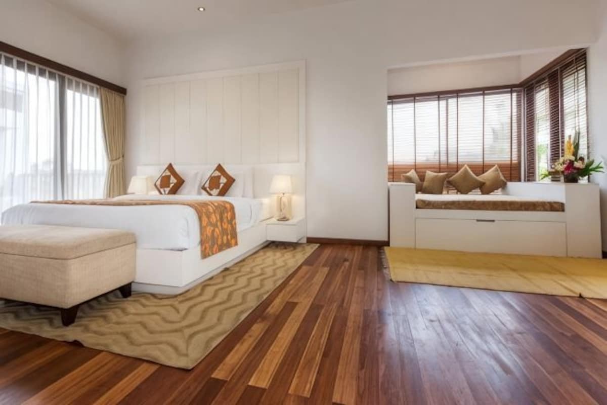 A hotel room with a bed, bedside tables, a sofa, and a window with blinds.