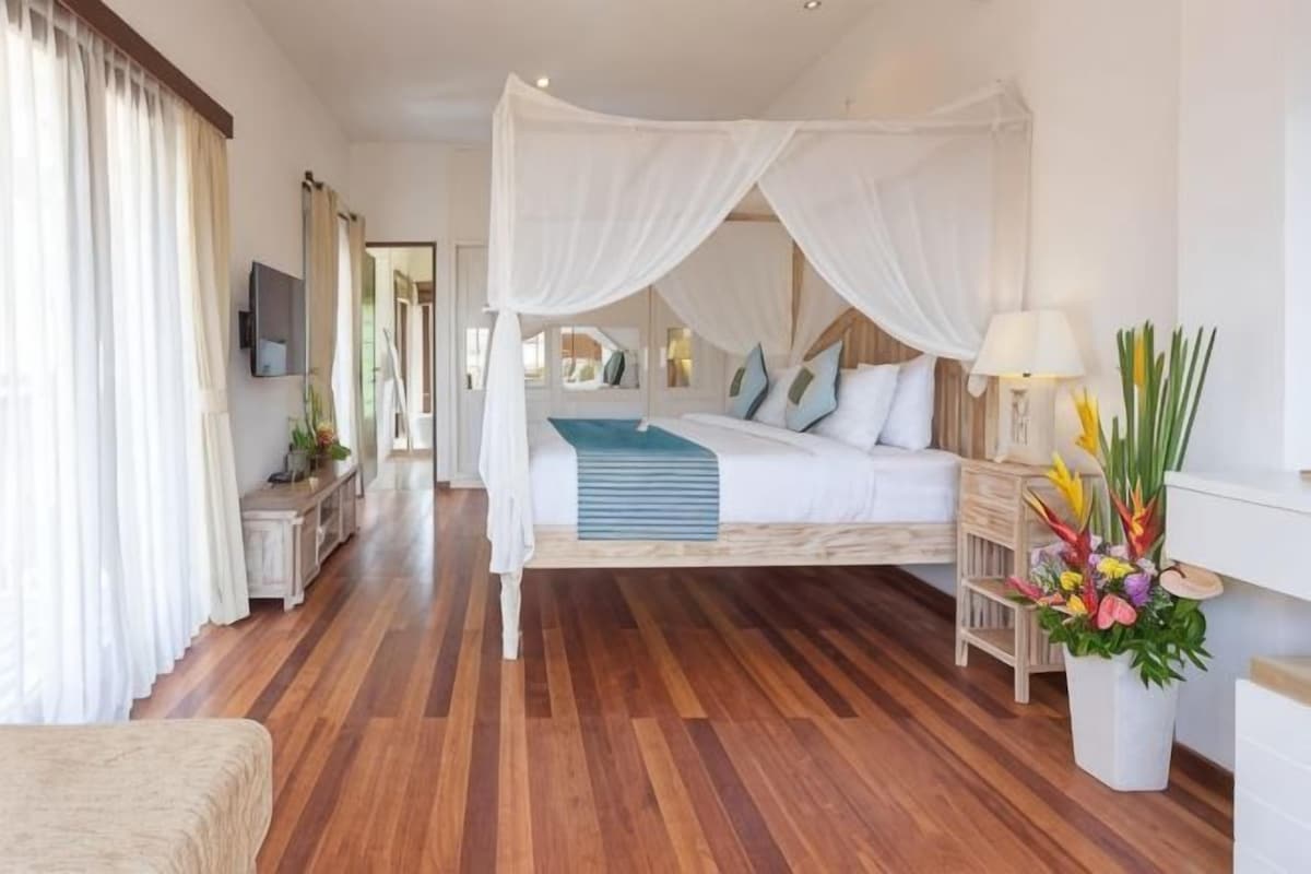 Une chambre à coucher avec un lit à baldaquin, une table de chevet avec une lampe, une plante en pot et un téléviseur fixé au mur.