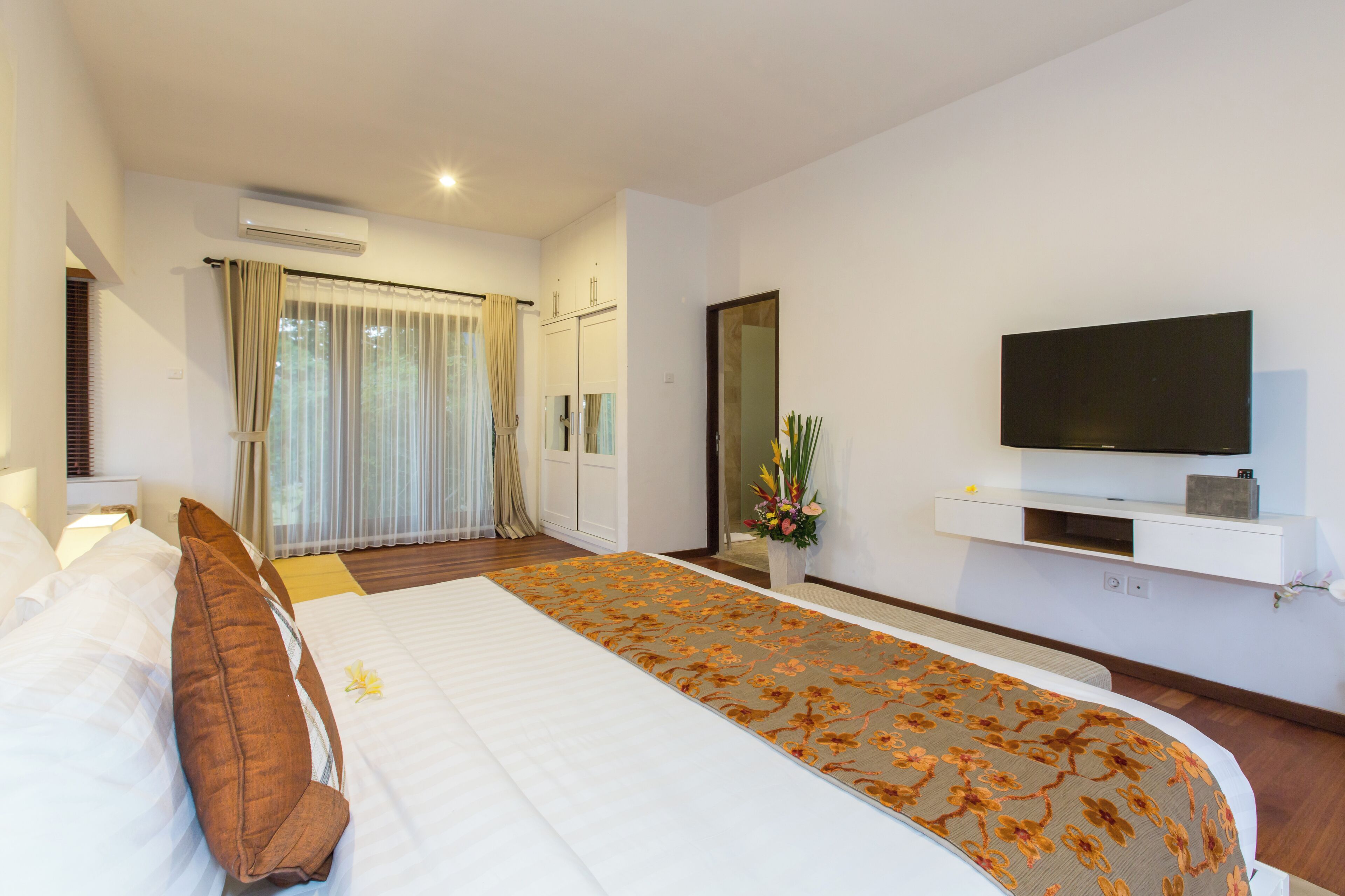 Una habitación de hotel moderna con una cama grande, un televisor de pantalla plana montado en la pared y un amplio ventanal con cortinas.