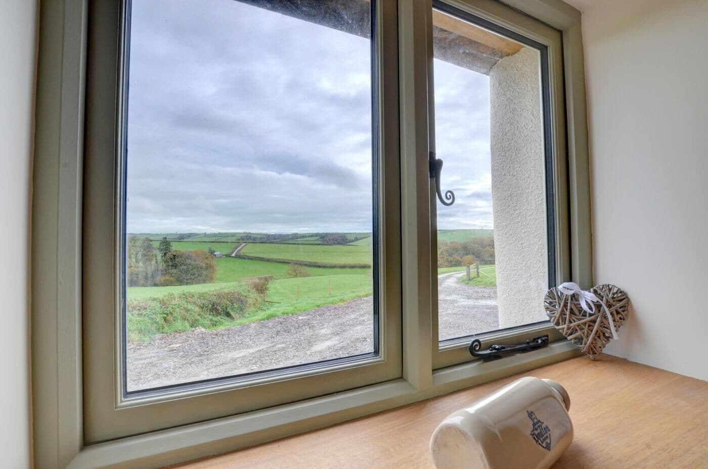 Una habitación con un ventanal grande que da a un paisaje rural, una mesa de madera y un adorno con forma de corazón.