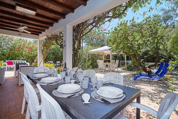 Un espace de restauration en plein air doté d’un patio couvert, de meubles en osier blancs et d’une table dressée pour un repas.