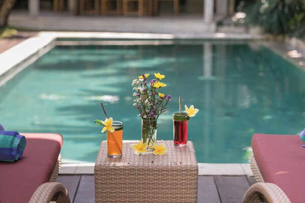 A poolside setting with lounge chairs, a wicker table, and drinks with flowers. - Villa Liang by Nagisa Bali (Seminyak)