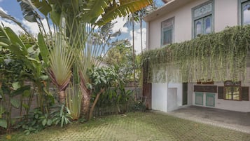 A courtyard with a paved floor, surrounded by lush greenery and a building with a white exterior and green shutters.