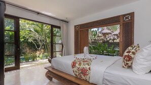 A bedroom with a large bed, a view of lush greenery, and a wooden ceiling design.