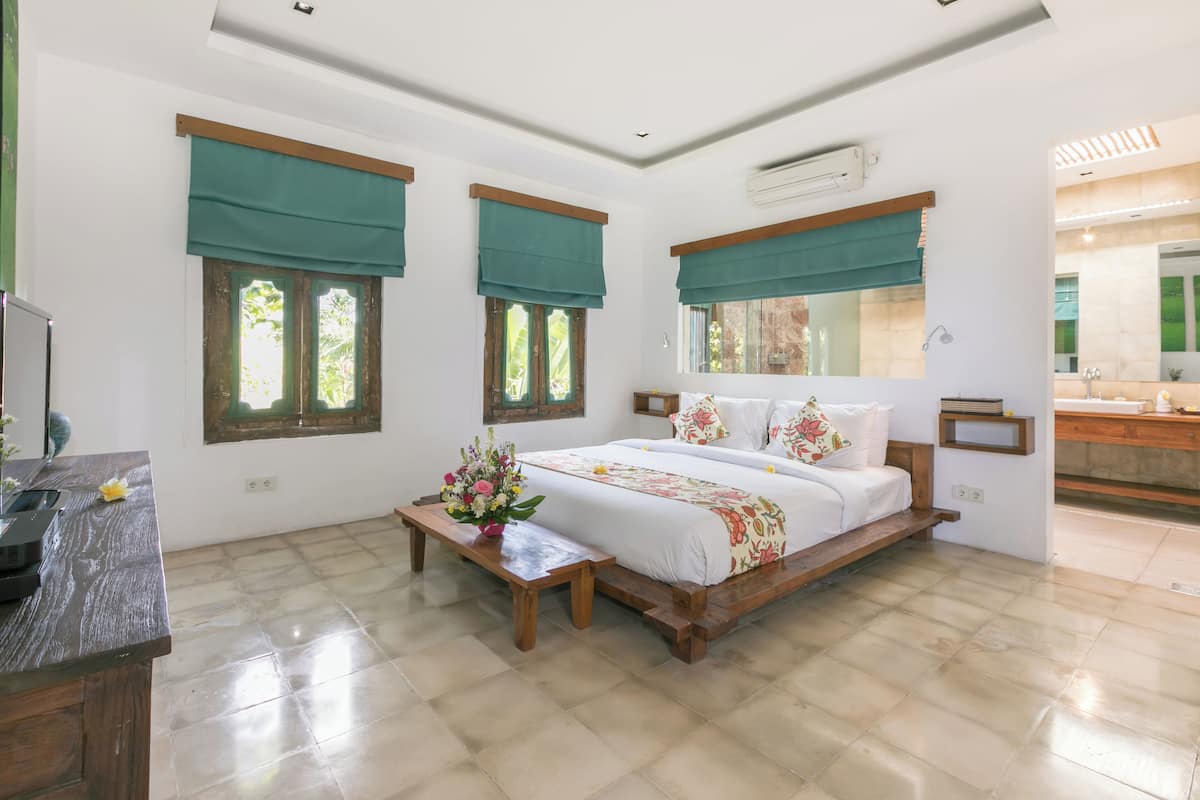 A spacious bedroom with a large bed, a wooden nightstand, a vanity with a mirror, and a window with a green curtain.