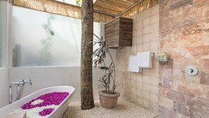 A bathroom with a bathtub filled with flowers, a potted plant, and a shower area.