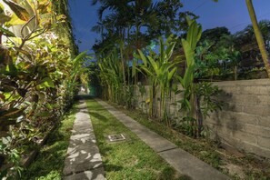 A narrow pathway flanked by lush greenery and a concrete wall, leading to a building entrance. - Villa Liang by Nagisa Bali (Seminyak)