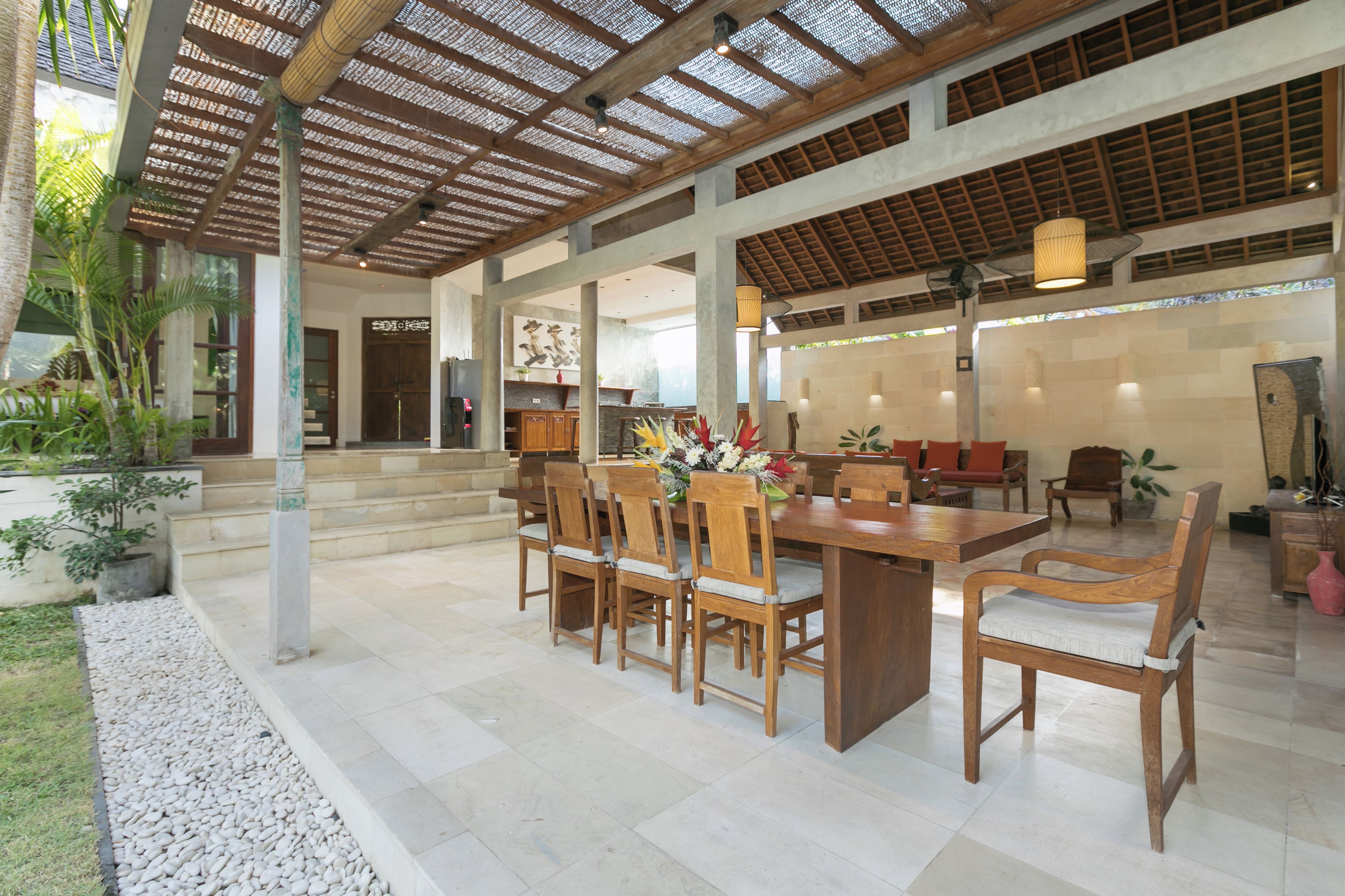 Un vaste espace intérieur doté d’une table à manger en bois entourée de chaises, d’un plafond avec une structure en bois et d’une vue sur l’extérieur.