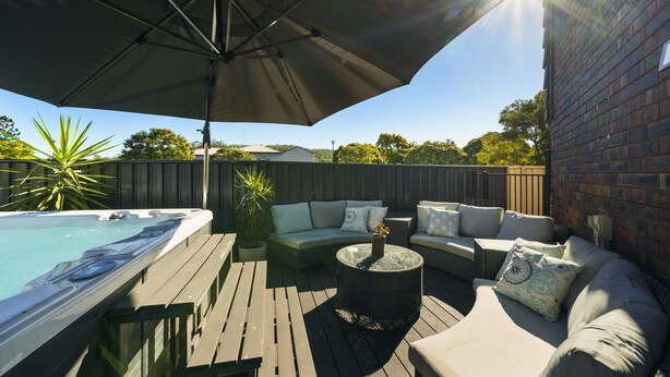 Um terraço com banheira de hidromassagem, área de estar externa e um grande guarda-sol.