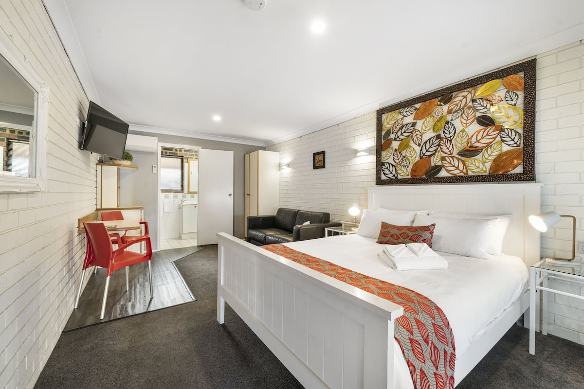 Une chambre d’hôtel comprenant un lit, un bureau avec une chaise, un canapé, un téléviseur fixé au mur et un grand motif décoratif en forme de feuilles sur le mur.