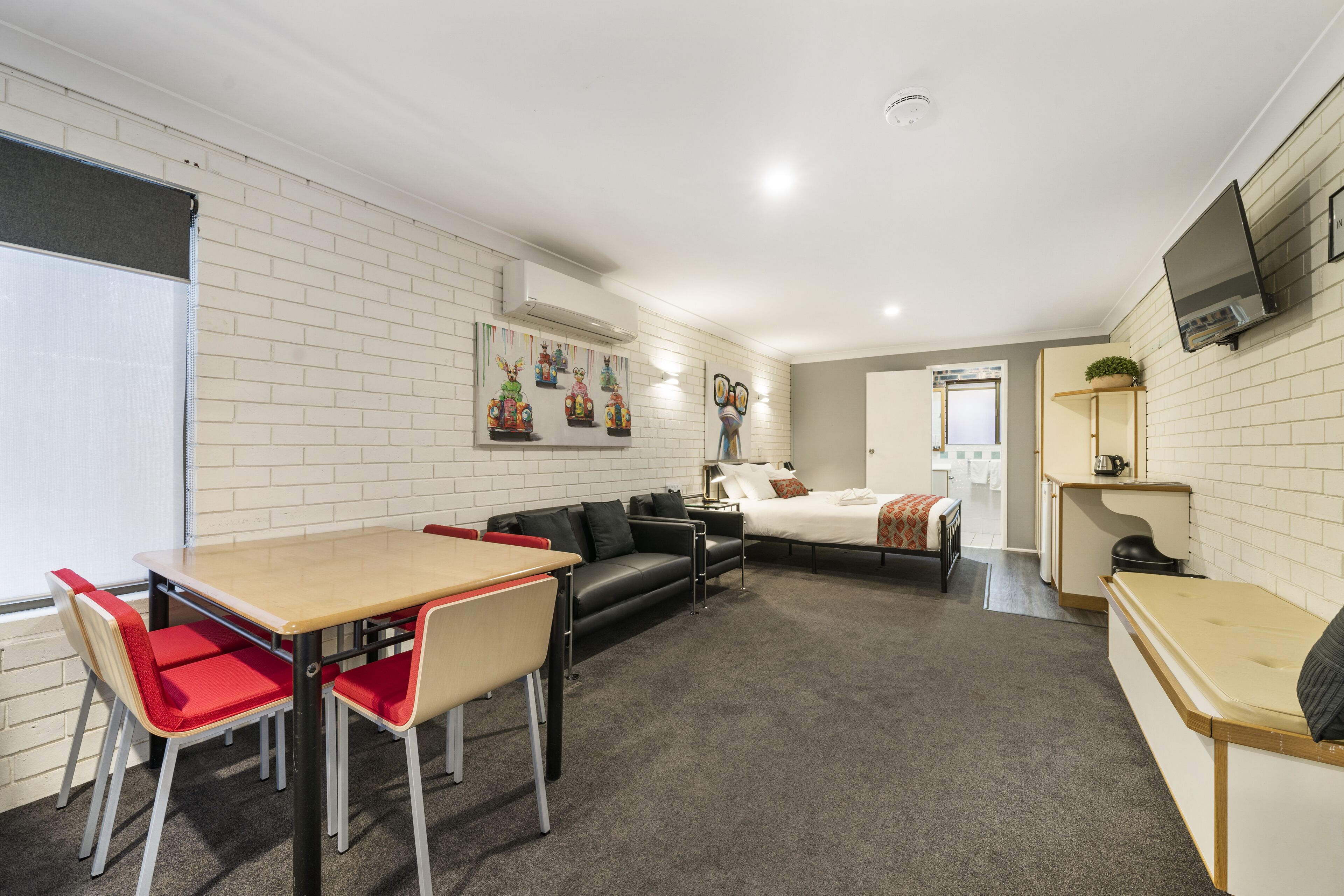 A compact room with a dining table, chairs, a sofa, a bed, and a kitchenette.