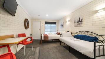 A small, well-lit room with two beds, a desk, and a TV.