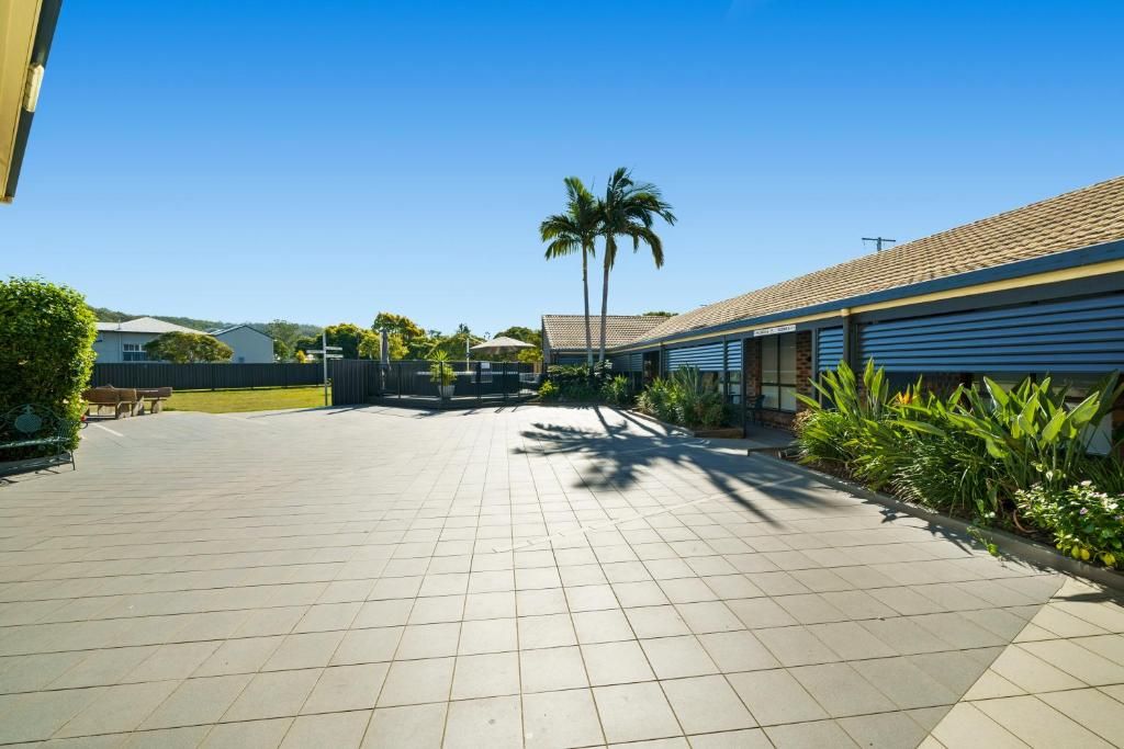 A paved courtyard with a palm tree, a fence, and a building with a tiled roof.